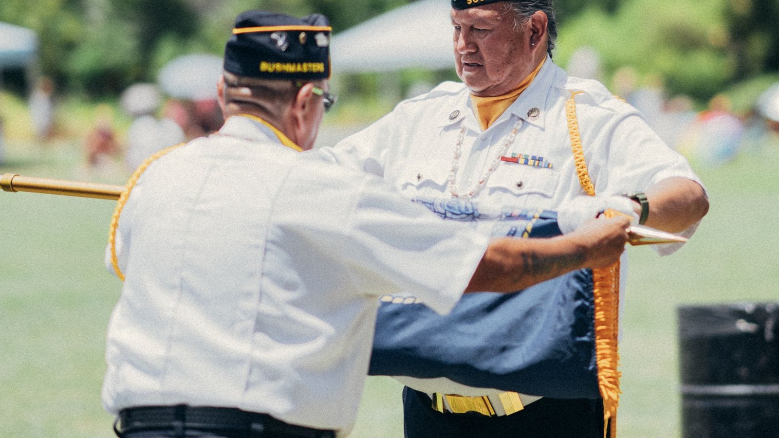 Two American Legion veterans carefully fold a ceremonial American flag during a sunny outdoor honor ceremony
