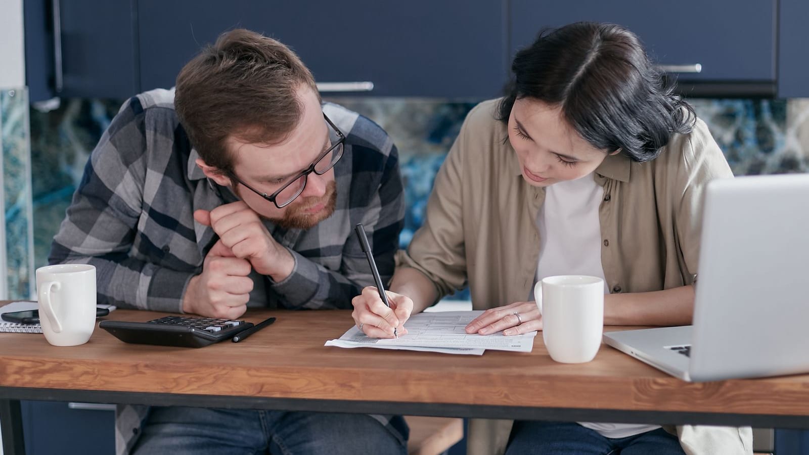 Couple sitting at a kitchen table reviewing financial documents together with a laptop and calculator