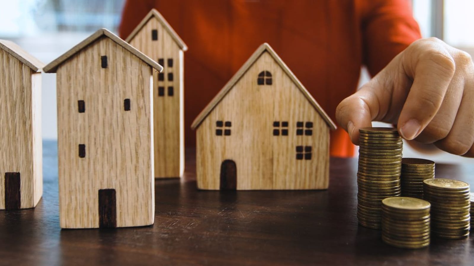 Stacks of coins beside small wooden model houses on a table, illustrating home savings and financing costs