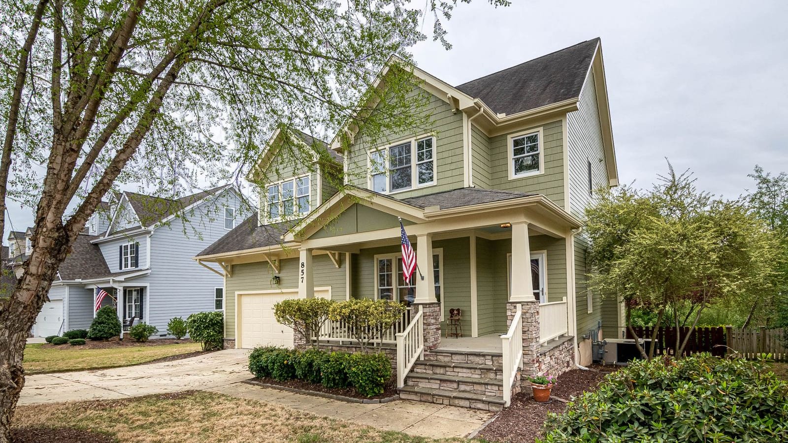 Welcoming two-story American suburban home with a covered front porch, manicured lawn, and an American flag under a bright blue sky