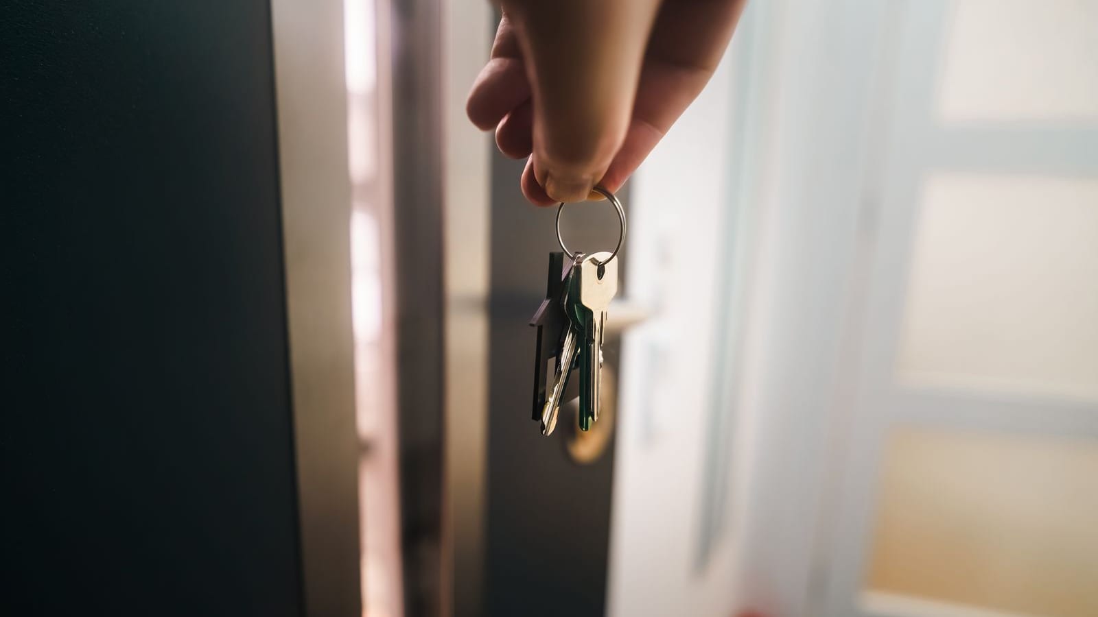A hand holding a set of house keys at the doorway of a new home, symbolizing homeownership